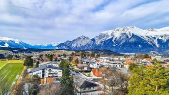 Panoramablick auf eine Siedlung mit schneebedeckten Bergen und weiten Feldern im Hintergrund.
