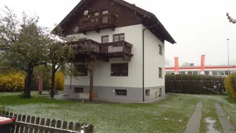 Freistehendes Haus mit weißer Fassade, Holzbalkonen und Garten, leicht mit Schnee bedeckt.