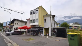 Gebäude mit Gewerbefläche im Erdgeschoss und Wohnungen darüber, umgeben von Bergen und einer Straße.