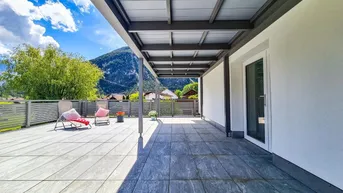 Geräumige, überdachte Terrasse mit Fliesenboden und Zugang zum Innenbereich, umgeben von Natur.