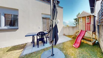 Garten mit gepflasterter Terrasse, Kinderspielhaus und weitem Blick auf die Berge.