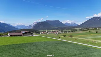 Weitläufige ländliche Landschaft mit grünen Feldern, Bergen im Hintergrund und einem Dorf in der Ferne.