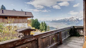 Rustikaler Holzbalkon mit traditionellem Geländer und weitem Blick auf die Berge.