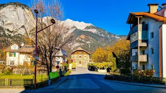 Panoramablick auf eine Berglandschaft mit Häusern und einer Straße im Vordergrund an einem sonnigen Tag.