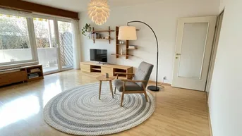 Helles Wohnzimmer mit Holzboden, modernem Sessel und Zugang zu einem sonnigen Balkon.