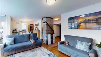 Gemütlicher Wohn-Essbereich mit Sofas, Esstisch und einem modernen Kaminofen auf Holzfußboden.