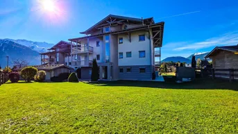 Mehrfamilienhaus mit gepflegter Rasenfläche und Bergblick unter strahlendem Himmel.