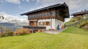 Traditionelles Holzhaus mit weißer Fassade und Bergblick, umgeben von einer grünen Wiese.