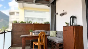 Gemütlicher Balkon mit Holzboden, Sitzgelegenheiten und Bergblick im Hintergrund.