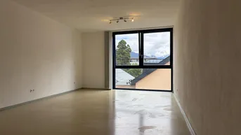 Helles, leeres Wohnzimmer mit großen Fenstern und Blick auf die umliegende Landschaft.