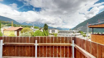 Sonniger Terrassenbereich mit Holzboden und Bergblick, umgeben von einer Holzumzäunung.