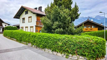 Traditionelles Haus mit weißer Fassade, Holzverkleidung und gepflegter Hecke in alpiner Umgebung.