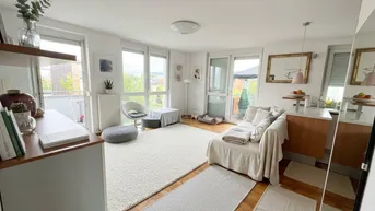 Heller offener Wohnbereich mit Holzboden, großen Fenstern und Zugang zum Balkon.