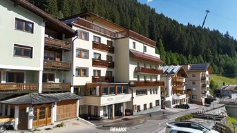 Hotelgebäude in den Bergen mit traditioneller Architektur und Balkonen, umgeben von grünen Wäldern.