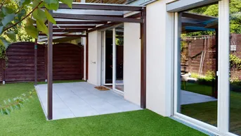 Gepflasterte Terrasse mit Pergola und kleinem Rasenbereich, direkt am Gebäude gelegen.