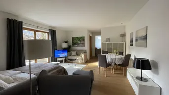 Heller Wohn- und Essbereich mit Parkettboden, Schlafsofa und Zugang zum Außenbereich.