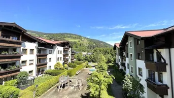 Blick auf die Wohnanlage mit Spielplatz und grünen Hügeln im Hintergrund unter blauem Himmel.