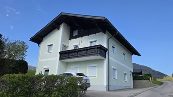 Traditionelles Haus mit hellgrüner Fassade, Satteldach und Balkon in ländlicher Umgebung.