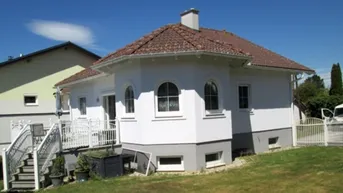 Weißes Einfamilienhaus mit Walmdach, Garten und Treppe zum Eingangsbereich.