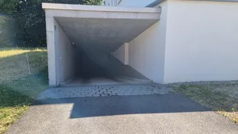 Eingang zu einer Tiefgarage oder einem überdachten Parkbereich mit Betonkonstruktion und asphaltierter Zufahrt.
