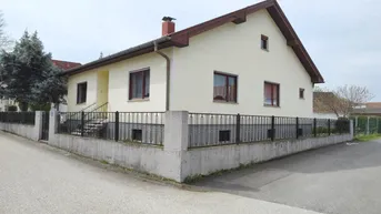 Einfamilienhaus mit heller Fassade, Satteldach und umzäuntem Vorgarten an einer Straßenecke.