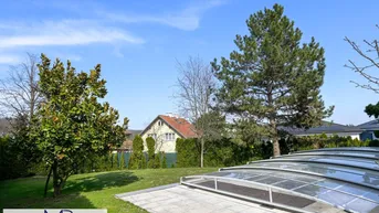 Großer Gartenbereich mit Rasenfläche, Bäumen und einer Abdeckung für den Pool unter blauem Himmel.