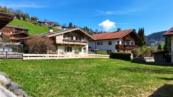 Traditionelle Häuser in alpiner Landschaft mit grünen Hügeln und blauem Himmel, umgeben von Natur.