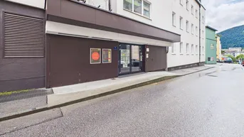 Eingangsbereich eines Geschäftsgebäudes mit brauner Fassadenverkleidung und großen Glastüren von der Straße aus gesehen.