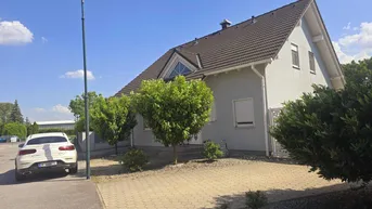 Modernes Einfamilienhaus mit Satteldach, gepflasterter Auffahrt und gepflegtem Vorgarten unter blauem Himmel.