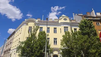Elegantes Altbaugebäude mit gelber Fassade, charakteristischer Architektur und hohen Fenstern unter blauem Himmel.