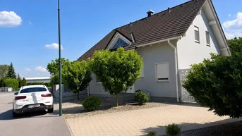 Modernes Einfamilienhaus mit gepflegtem Vorgarten und gepflasterter Auffahrt unter blauem Himmel.