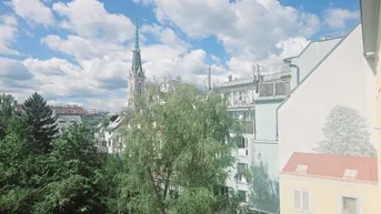 Blick aus dem Fenster auf die Stadt mit Kirchturm, Bäumen und umliegenden Gebäuden.