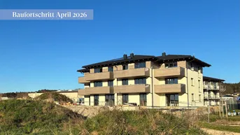 Neubau-Mehrfamilienhaus im Baufortschritt, aufgenommen im April 2026, mit Balkonen und Solaranlage auf dem Dach.