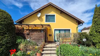Gelbes Einfamilienhaus mit Satteldach, Vorgarten und überdachtem Eingangsbereich unter blauem Himmel.