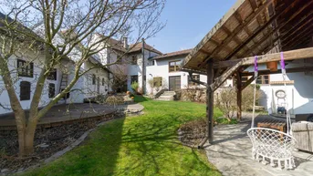 Großer Gartenbereich mit Rasenfläche, Schaukel und überdachtem Sitzplatz vor dem Wohnhaus.