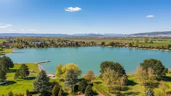Panoramablick auf den See, die umliegende Landschaft und ferne Berge unter blauem Himmel.