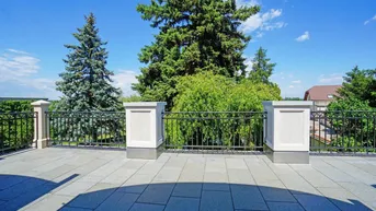 Geräumige Terrasse mit Fliesenboden, Metallgeländer und Blick ins Grüne unter blauem Himmel.