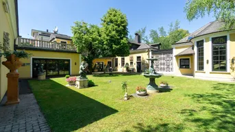 Sonniger Innenhof mit gepflegtem Rasen, Springbrunnen und dekorativen Statuen umgeben von Gebäuden.