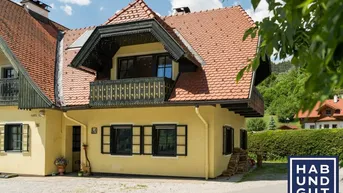 Traditionelles Haus mit gelber Fassade, rotem Ziegeldach und Holzbalkon in alpiner Umgebung.