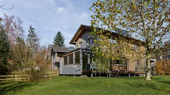 Modernes Holzhaus mit großem Garten und Bäumen unter blauem Himmel.