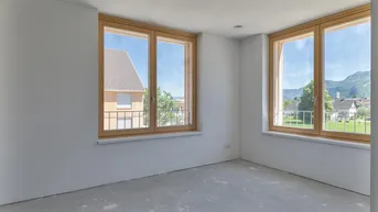 Heller, unmöblierter Raum mit großen Holzfenstern und Blick auf die umliegende Landschaft und Berge.