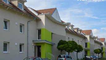 Moderne Reihenhäuser mit hellen Fassaden, grünen Akzenten und Satteldächern unter blauem Himmel.