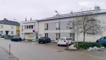 Gebäudeansicht von der Straße mit parkenden Autos, moderner Architektur und leichter Schneedecke.