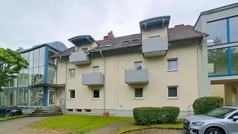 Mehrfamilienhaus mit mehreren Balkonen, einer modernen Glasfassade und gepflegter Grünanlage.
