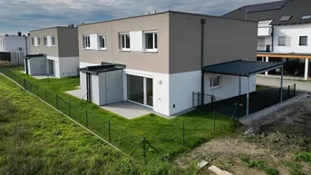 Moderne Reihenhäuser mit schlichter Fassade, kleinen Gärten und überdachten Stellplätzen in einer Wohnsiedlung.