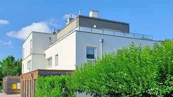Moderne Wohnanlage mit weißer Fassade, Flachdach und grüner Hecke unter blauem Himmel.