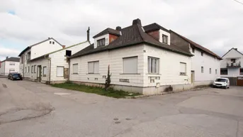 Altes Wohnhaus mit weißer Fassade und Rollläden an einer Straßenecke.