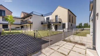 Moderne Wohnanlage mit mehreren Gebäuden und begrünten Außenbereichen unter blauem Himmel.