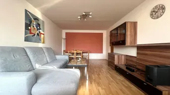 Geräumiger Wohn-Essbereich mit hellem Parkettboden, bequemer Couch und Essbereich im Hintergrund.