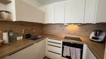 Funktionale Küche mit weißen Schränken, Holzoptik-Arbeitsplatte und integriertem Kochfeld.